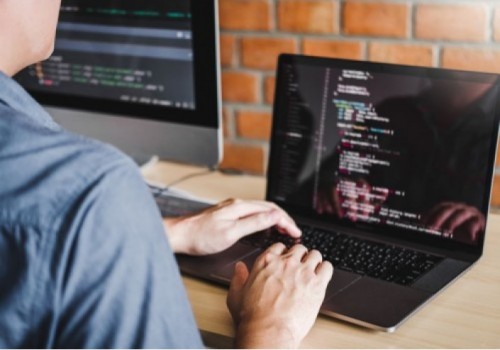 Imagem 2 - apresenta um homem branco com camisa azul, utilizando um notebook, programando em linguagem de código.